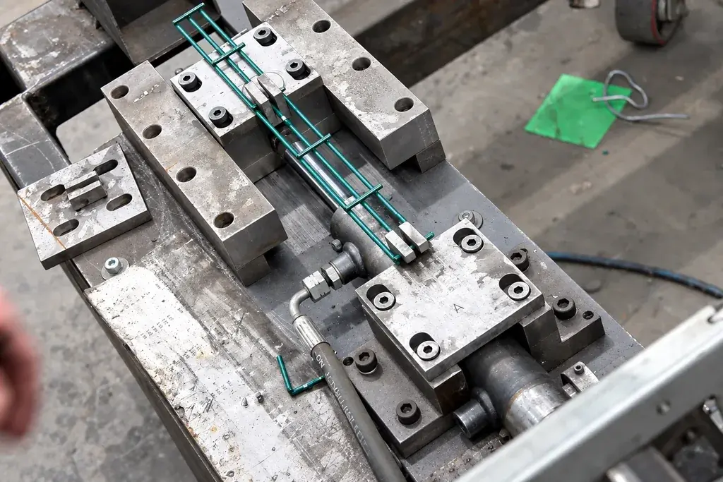 Green welded mesh specimen secured between metal clamps in a test fixture