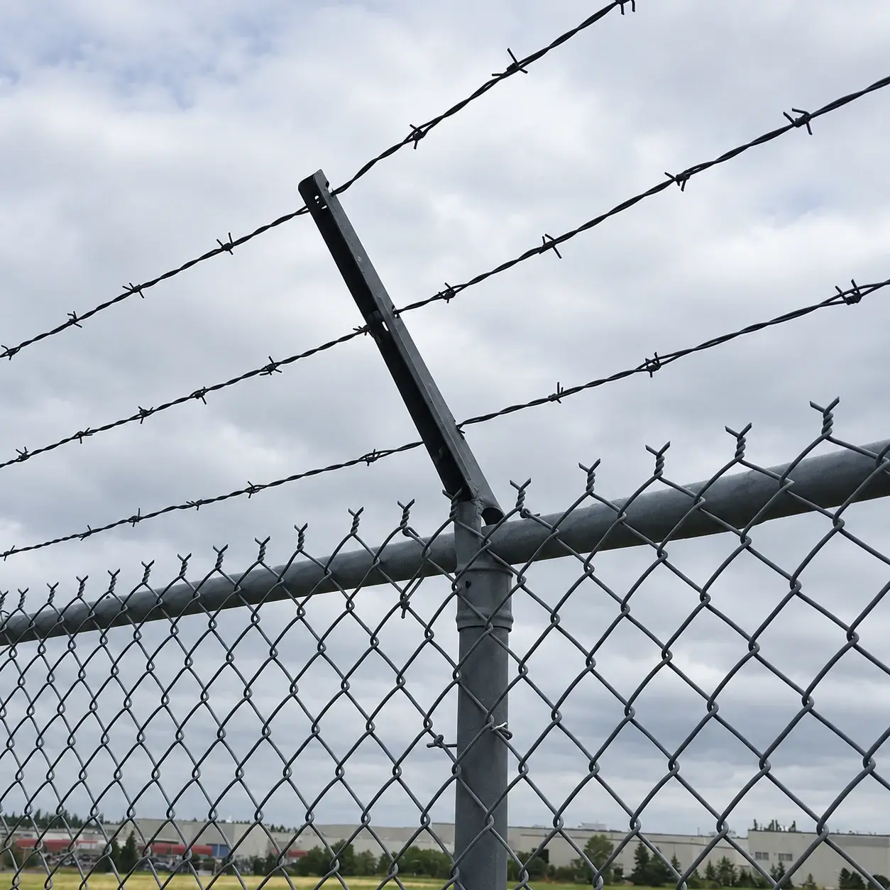 Chain link mesh tied to a post and top rail with a barbed-wire extension above