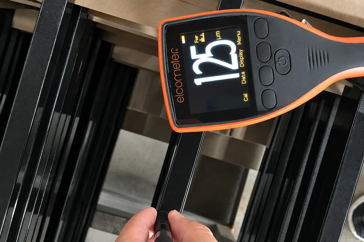 Handheld coating gauge checking a black steel fence rail
