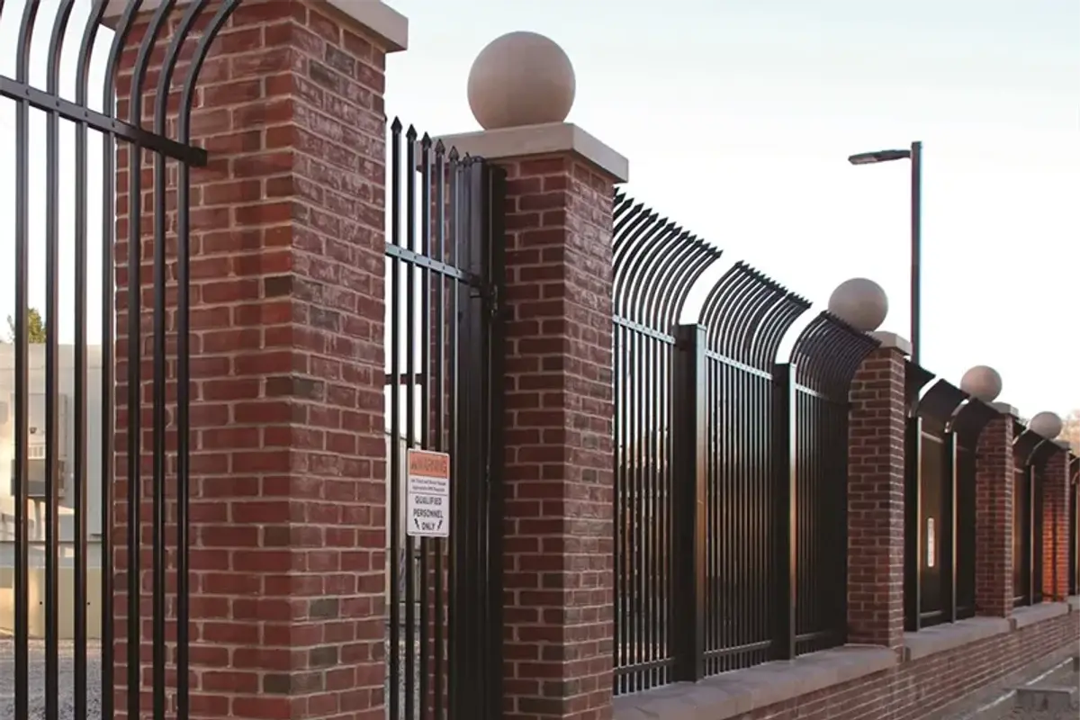 Black steel fence and gate joined to brick piers along a low wall