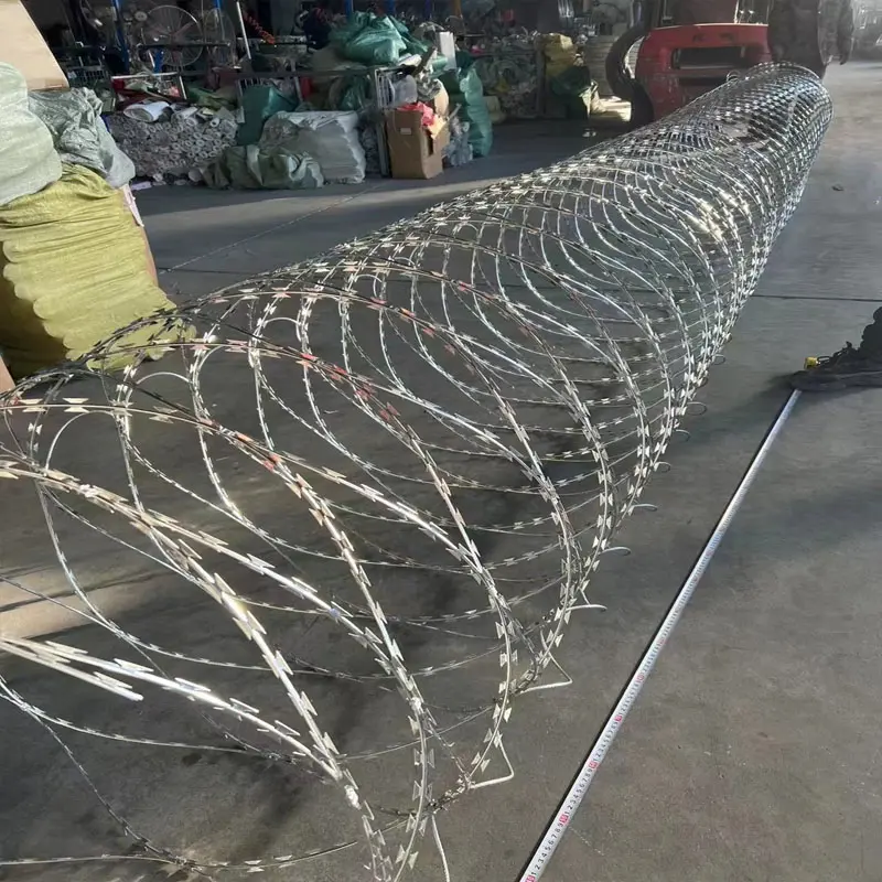 Concertina razor wire coil extended along a workshop floor beside a tape measure