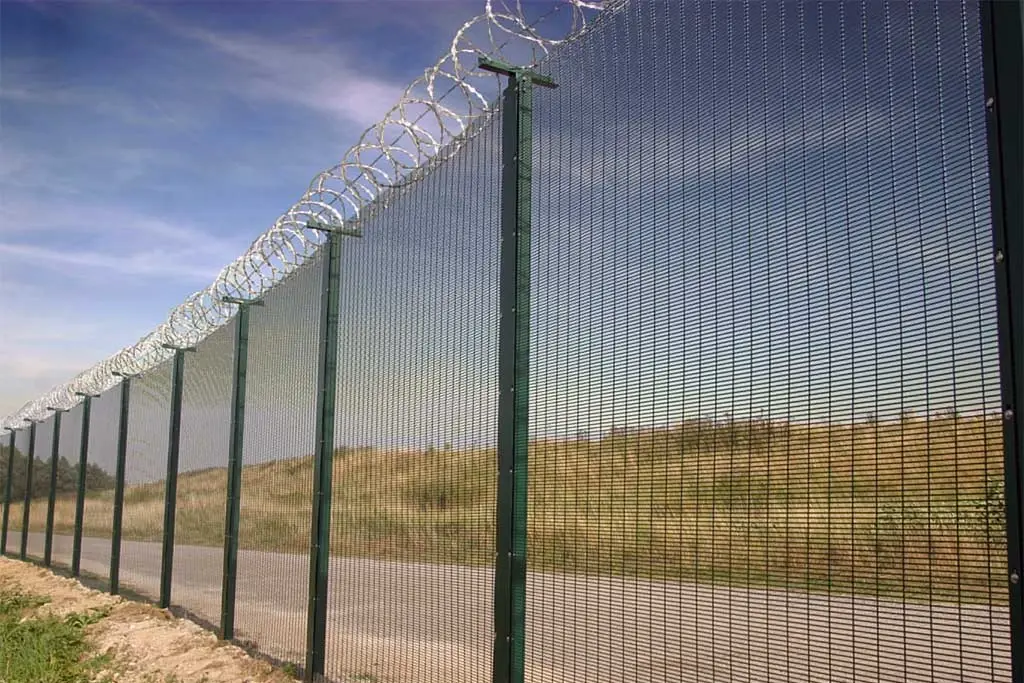 Concertina razor wire installed along the top of a tall mesh security fence