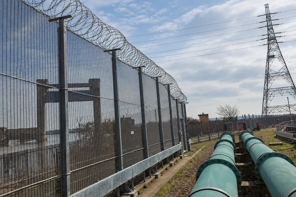Tall dark mesh perimeter fence beside an industrial service corridor.