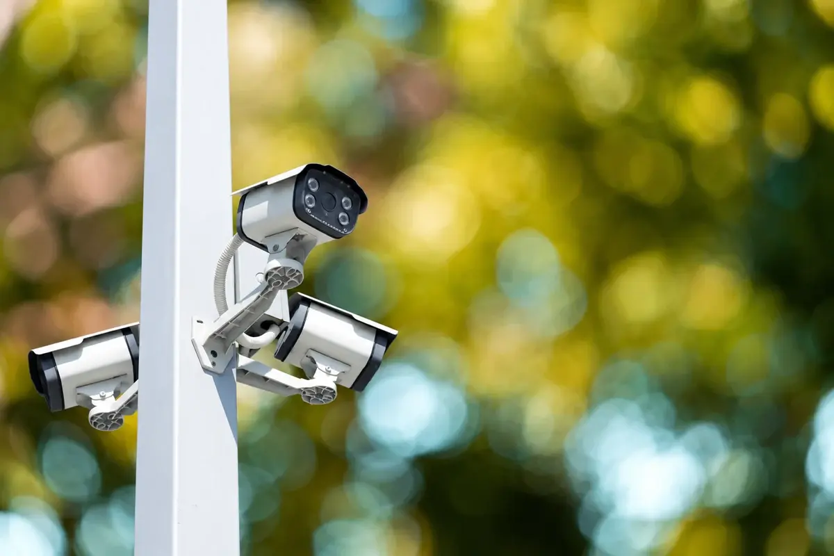 Three surveillance cameras mounted to a white post.