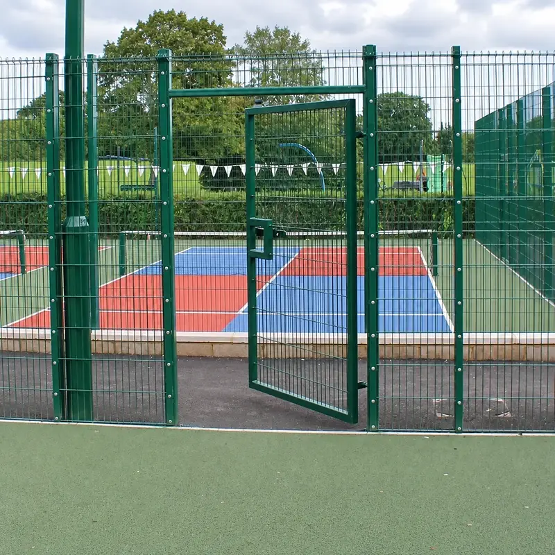 Open green twin-wire pedestrian gate at a sports court