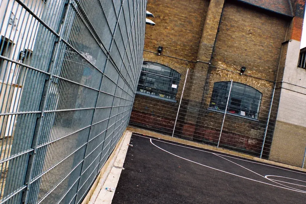 Twin wire sports fence panel and post beside a court wall