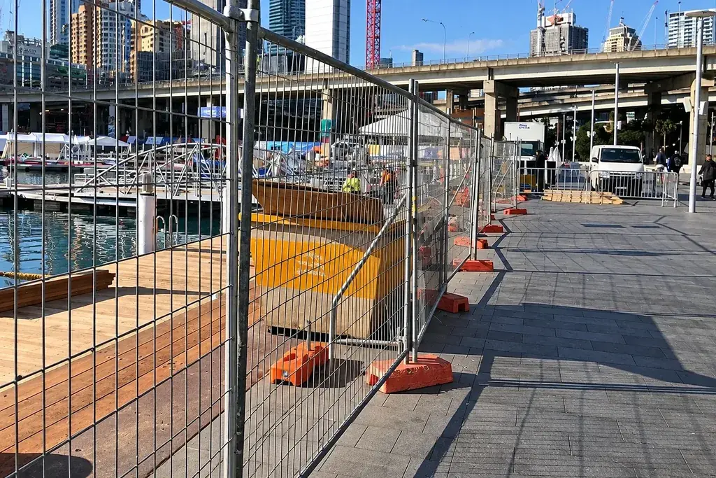 Temporary welded mesh fence panels with visible support feet beside a paved route