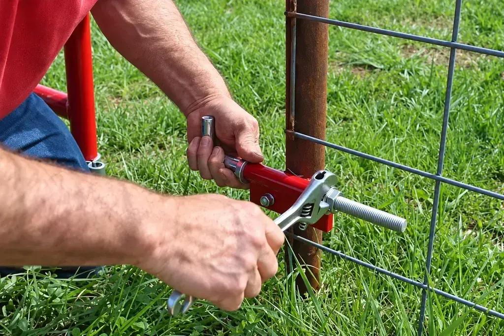Installer adjusting a farm gate hinge connection beside a fence post