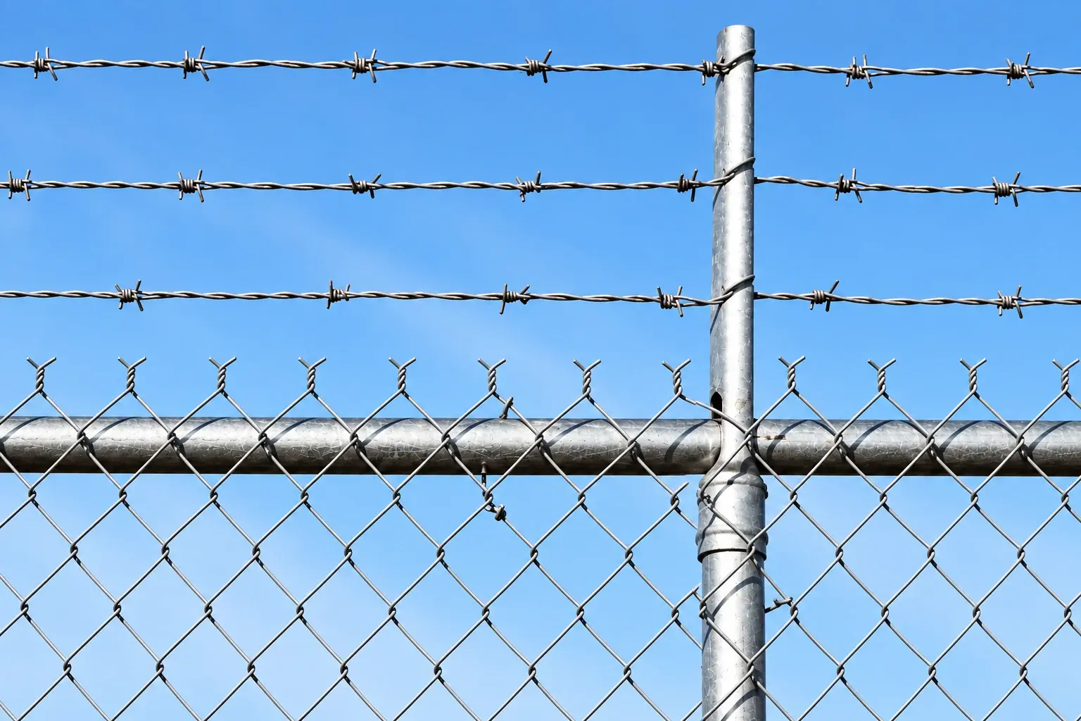 Three barbed wire strands on a post extension above chain link mesh