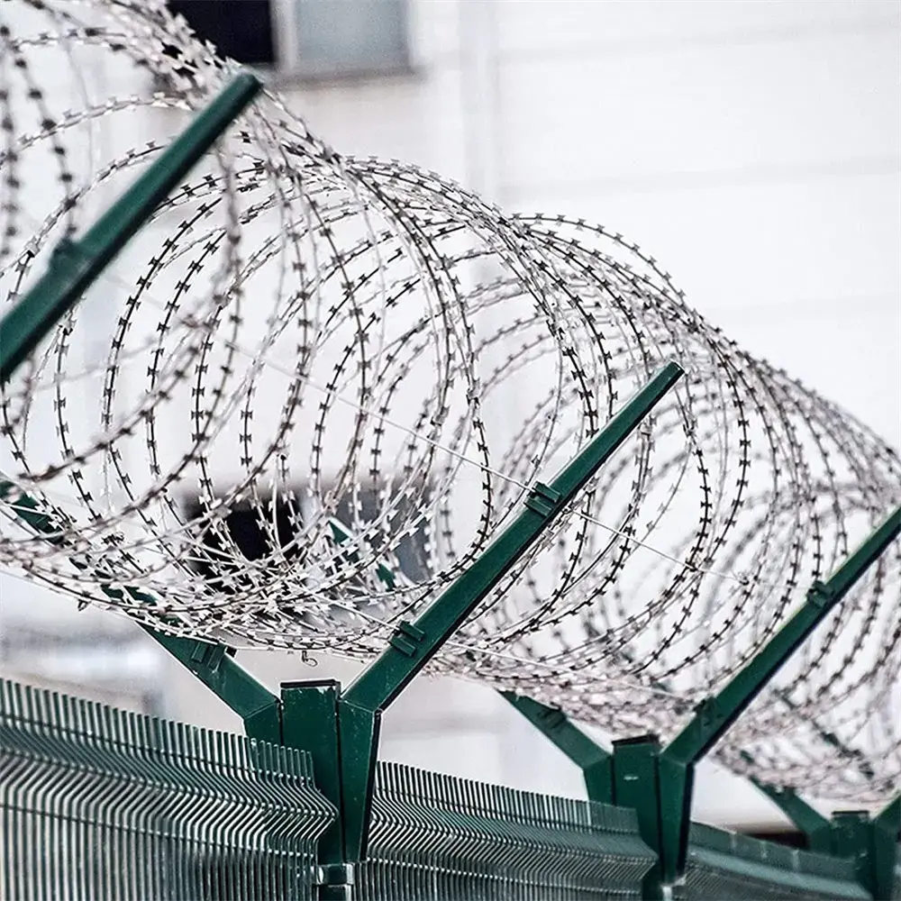 Angled steel brackets supporting razor wire above a mesh fence