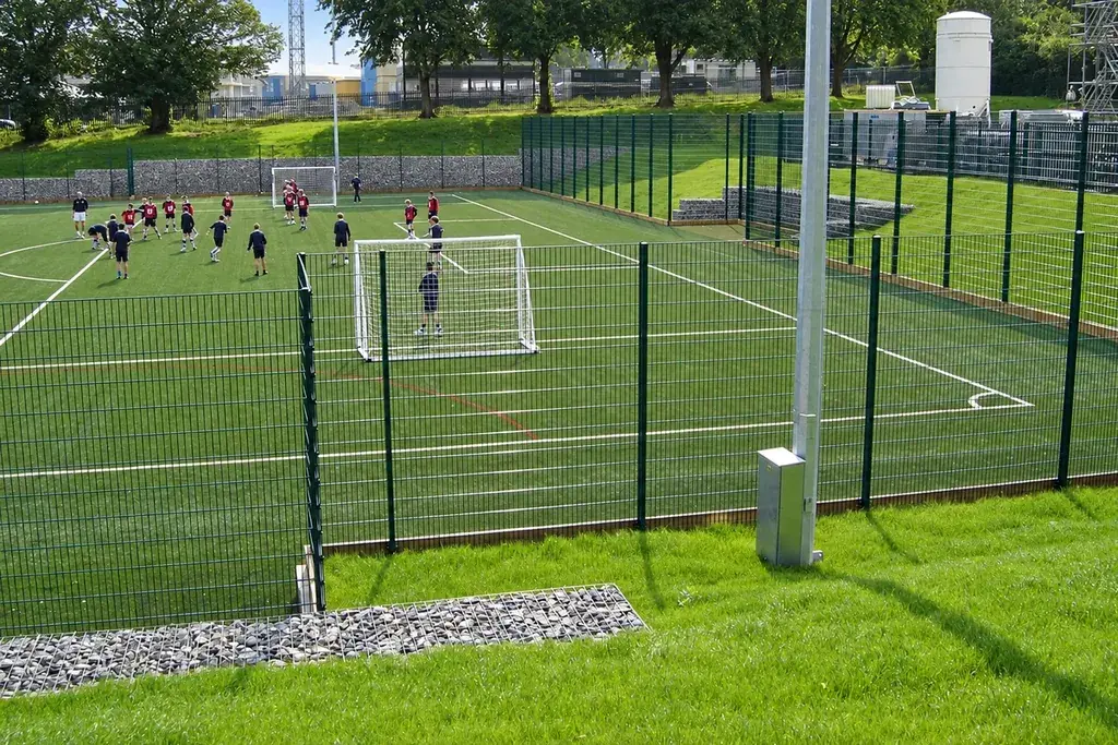 Green mesh fencing around a football pitch with a goal visible.