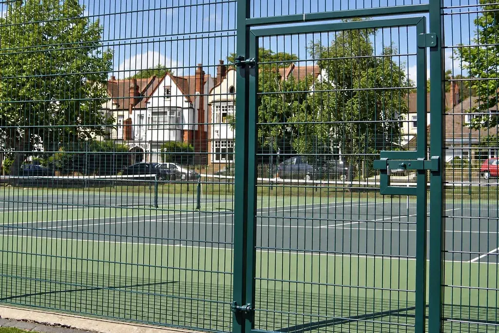 Green pedestrian mesh gate in a sports court boundary.