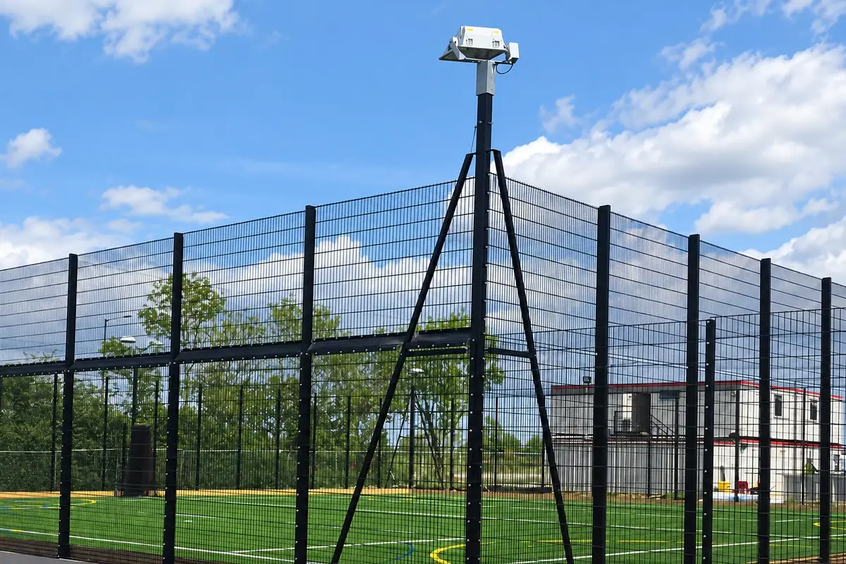 Tall mesh sports enclosure with separate supported lighting posts.
