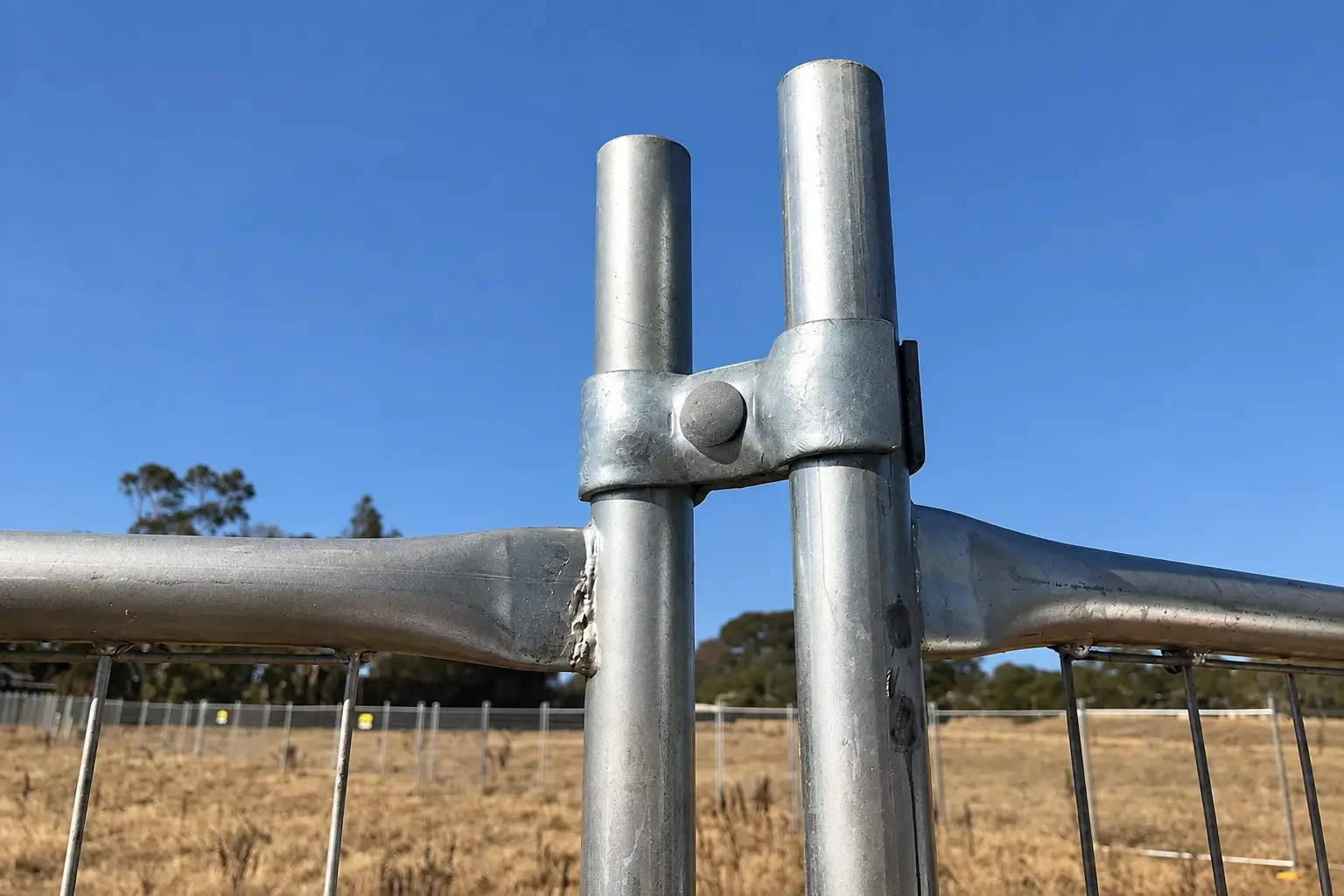 Galvanised clamp joining two round temporary fence posts