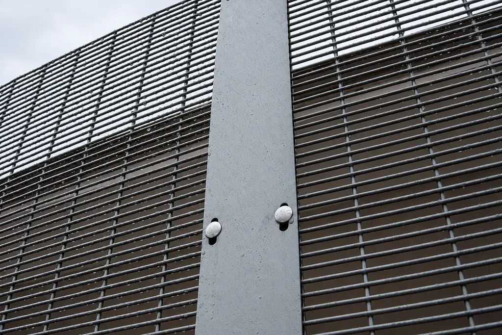 Close-spaced mesh secured to a steel post with a clamp bar and bolts