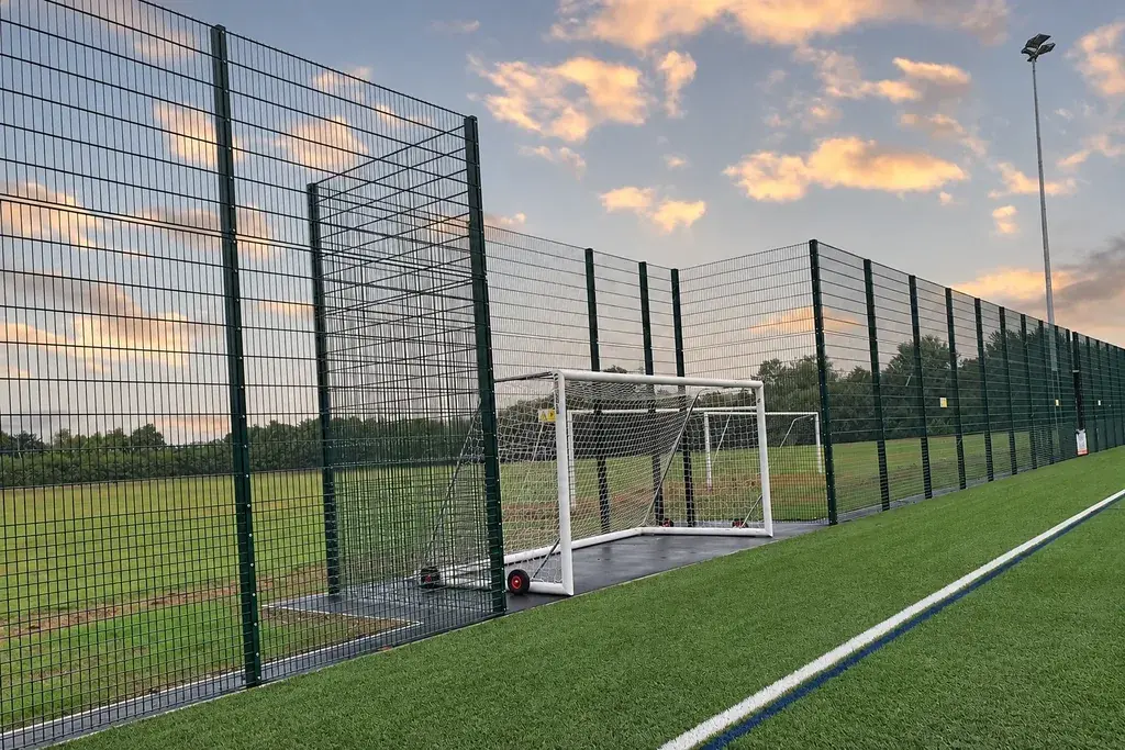 Tall mesh fencing with a recessed football goal on an artificial pitch