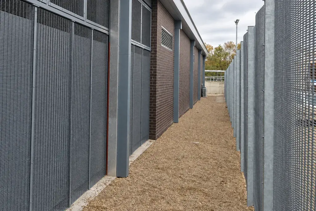 Tall metal mesh fencing along the side of an industrial building.