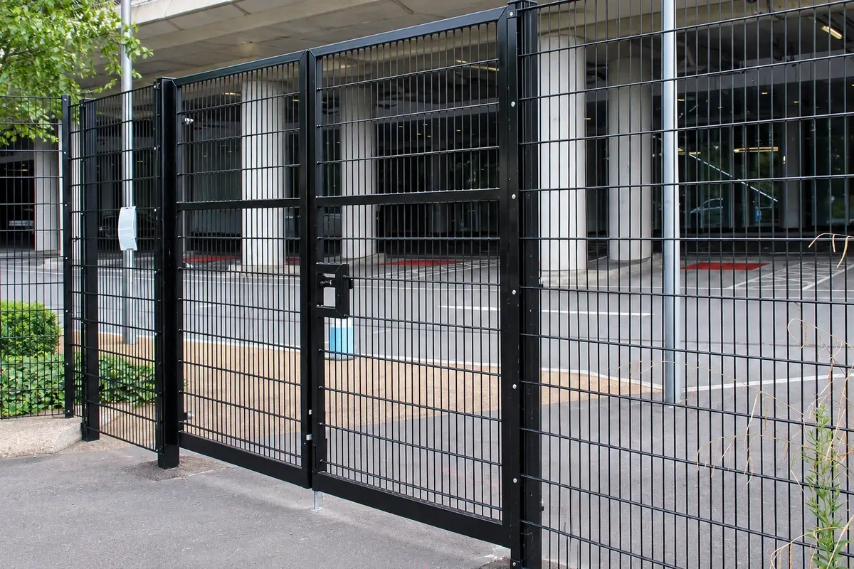 Black double-leaf mesh vehicle gate at a paved entrance.