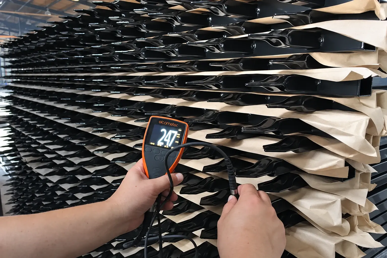 Handheld inspection instrument beside stacked black steel fence panels