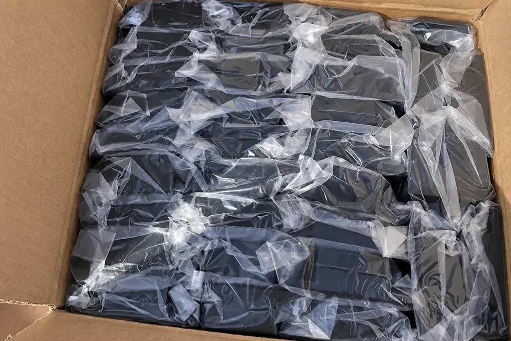 Black metal fence post brackets packed in clear bags inside a carton