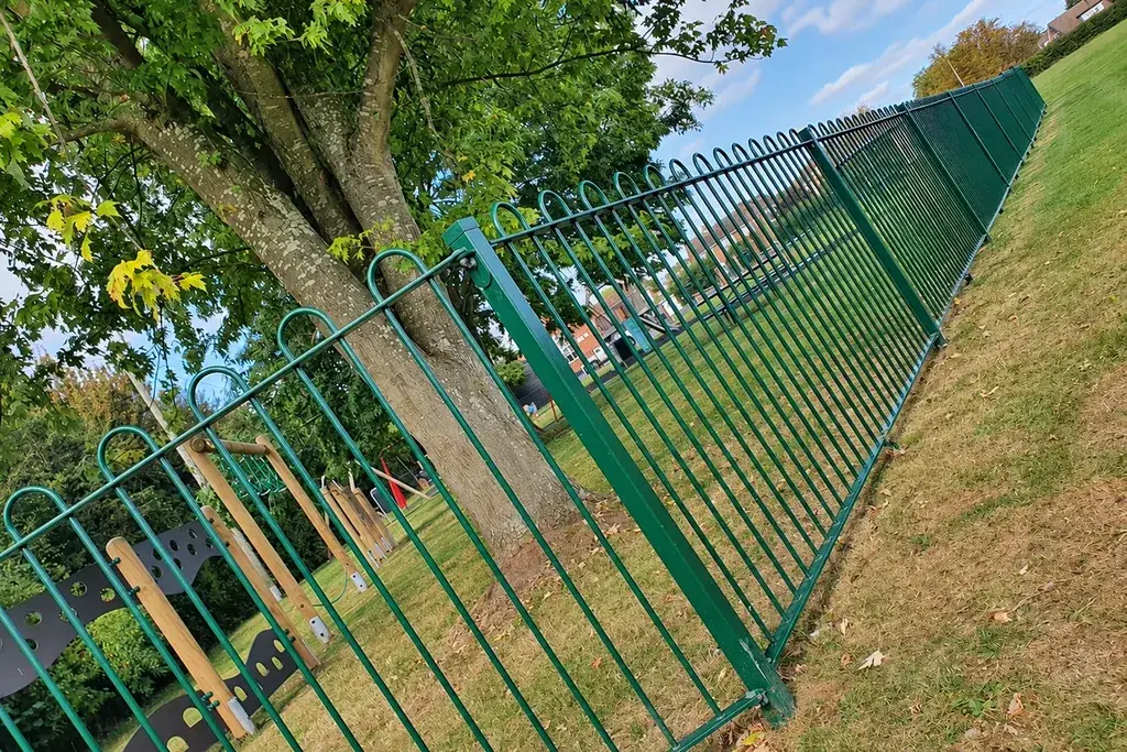 Green bow top railing panels and posts following a sloping park boundary.