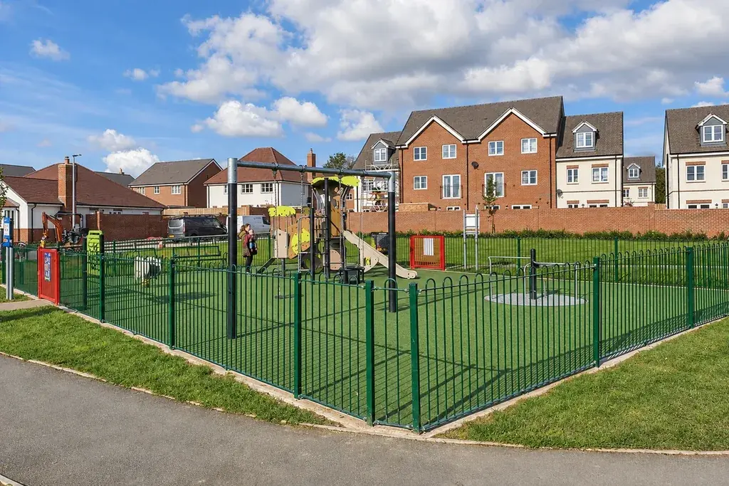 Green bow top railings around a playground with play equipment.