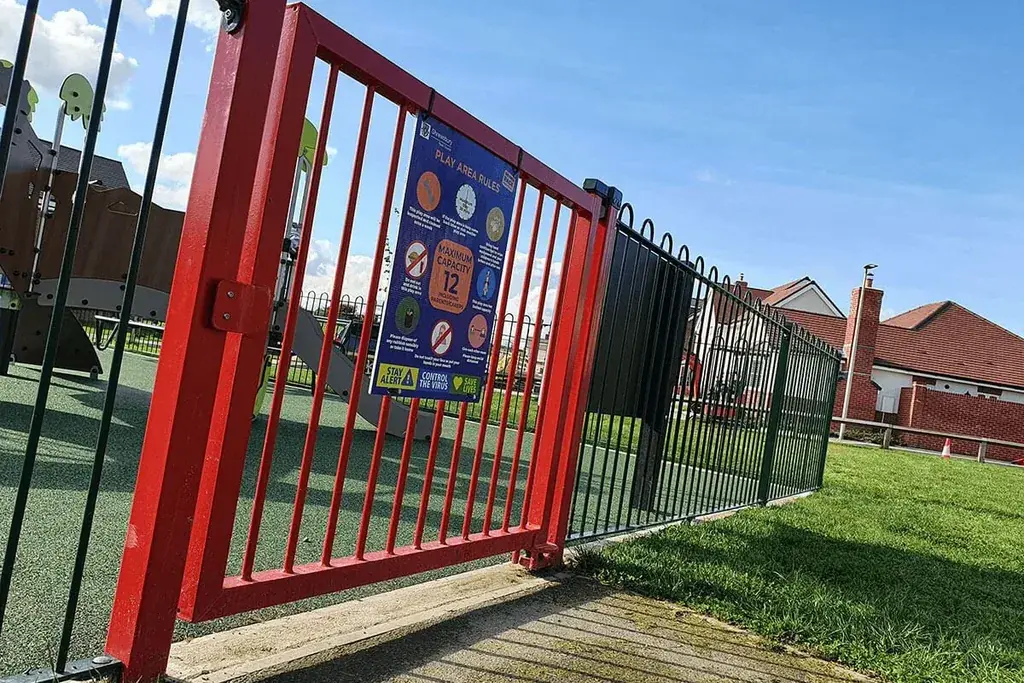 Red pedestrian gate within a green playground railing boundary.