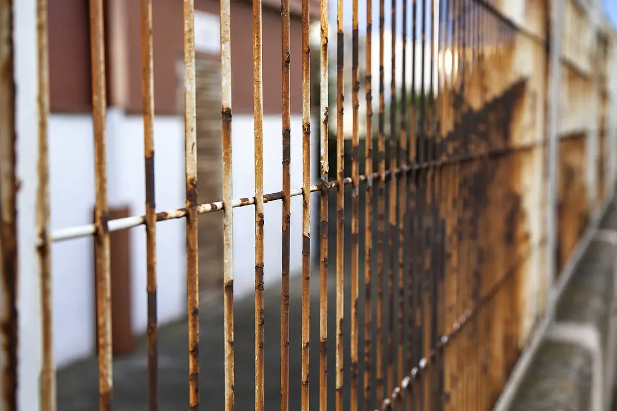 Close view of corrosion on a coated metal fence.