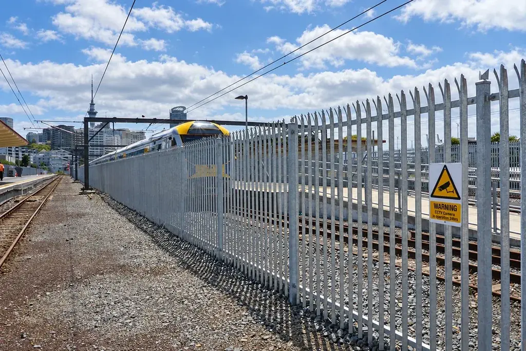 Metal palisade vehicle gate within a long industrial fence.