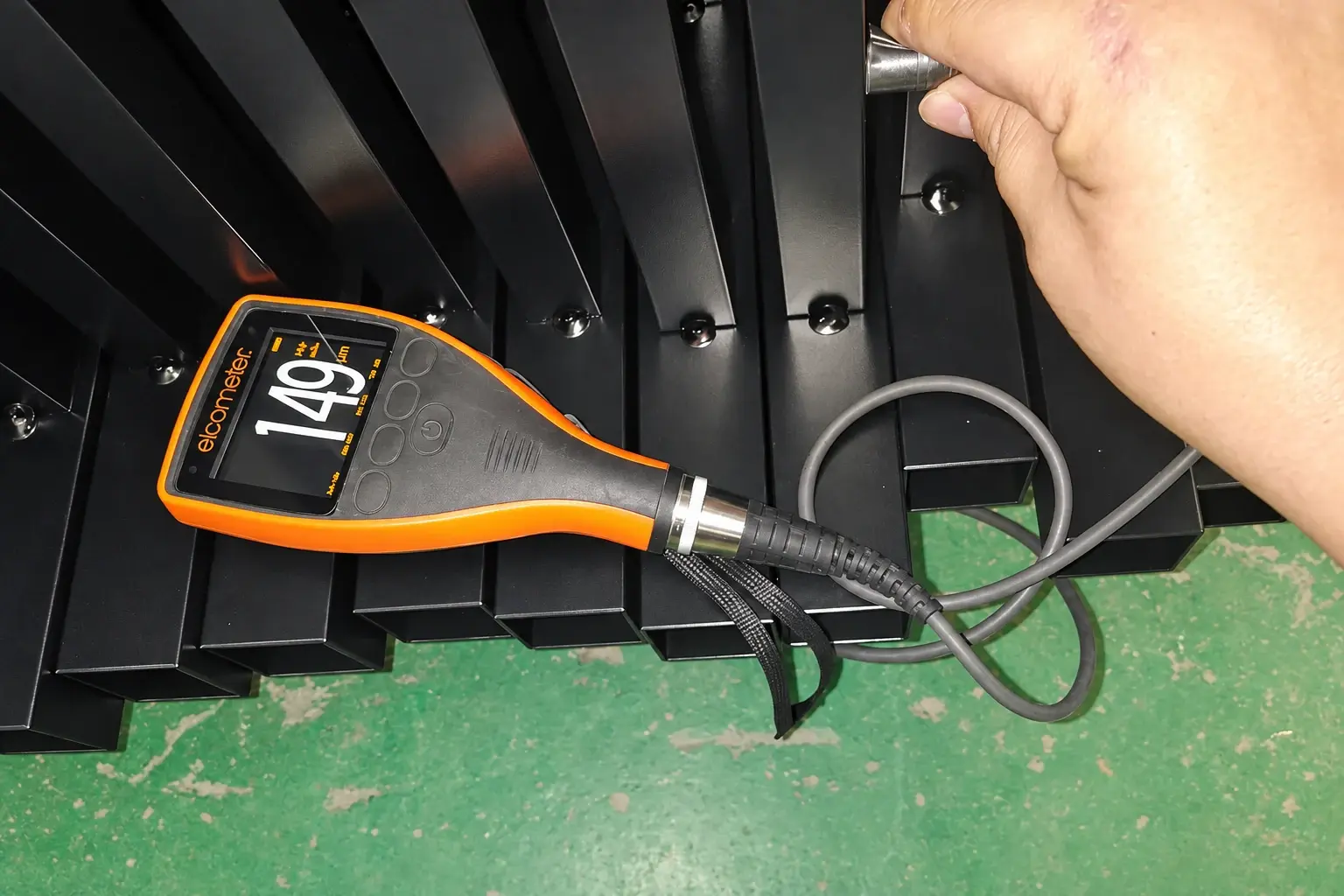 Coating-thickness gauge and probe checking a black metal frame