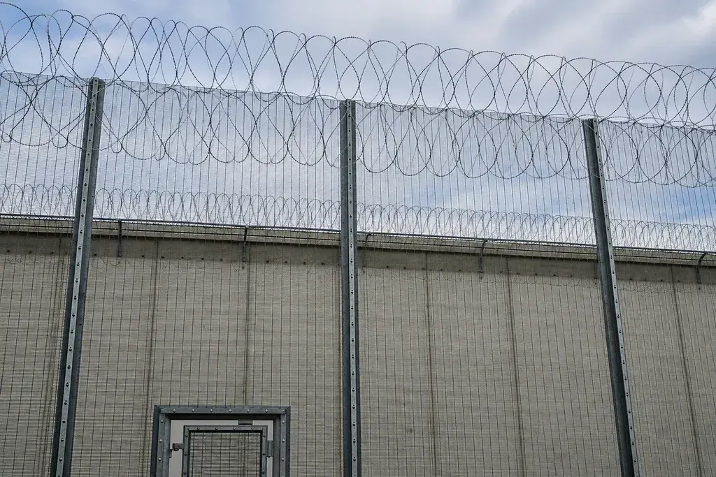 Tall security mesh fence with posts and coiled wire topping in front of a building