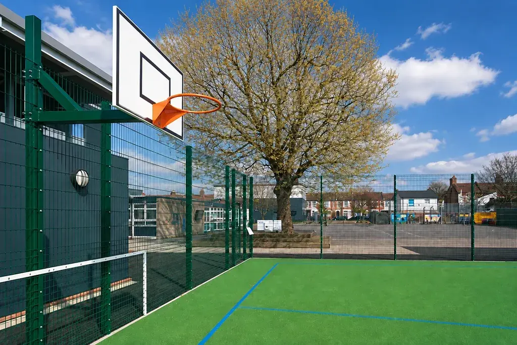 Green fenced sports court with a basketball hoop and court markings