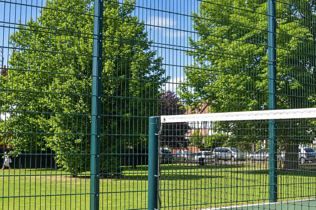 Green welded mesh fencing behind a tennis court net