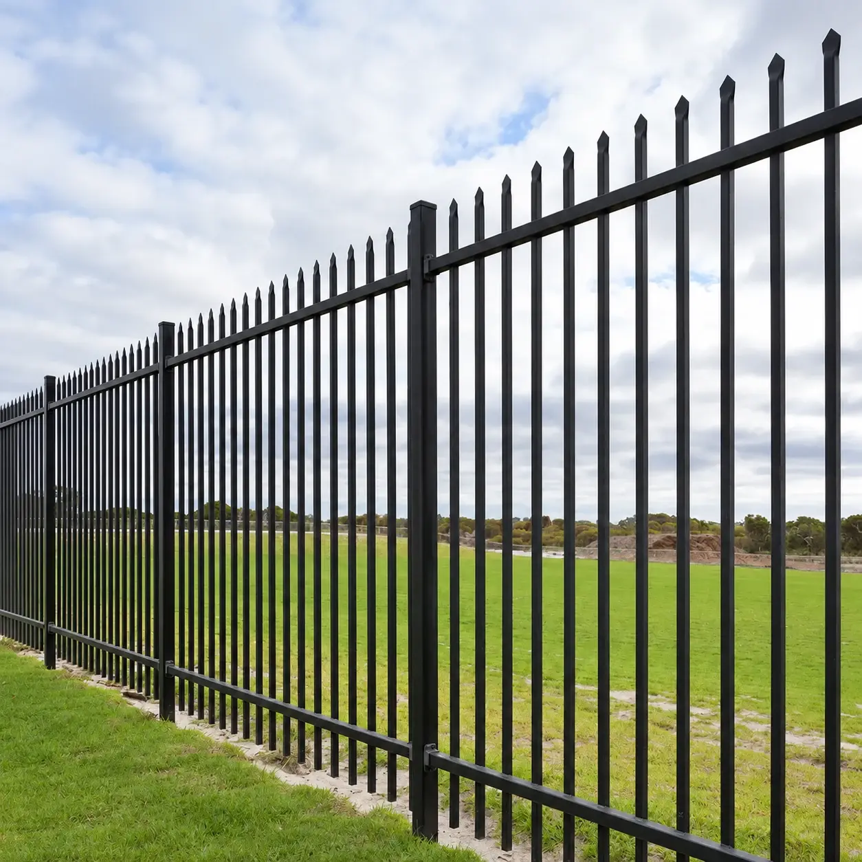 Black tubular steel fence with spear-top pickets beside grass