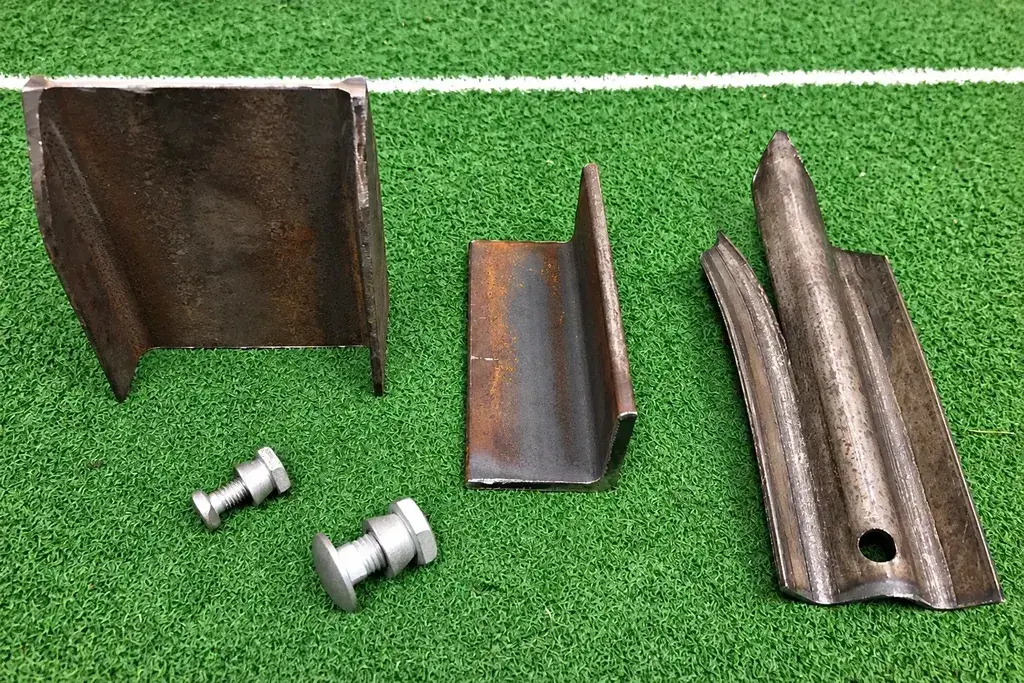 Steel section samples, a formed palisade pale and two bolts on a green surface