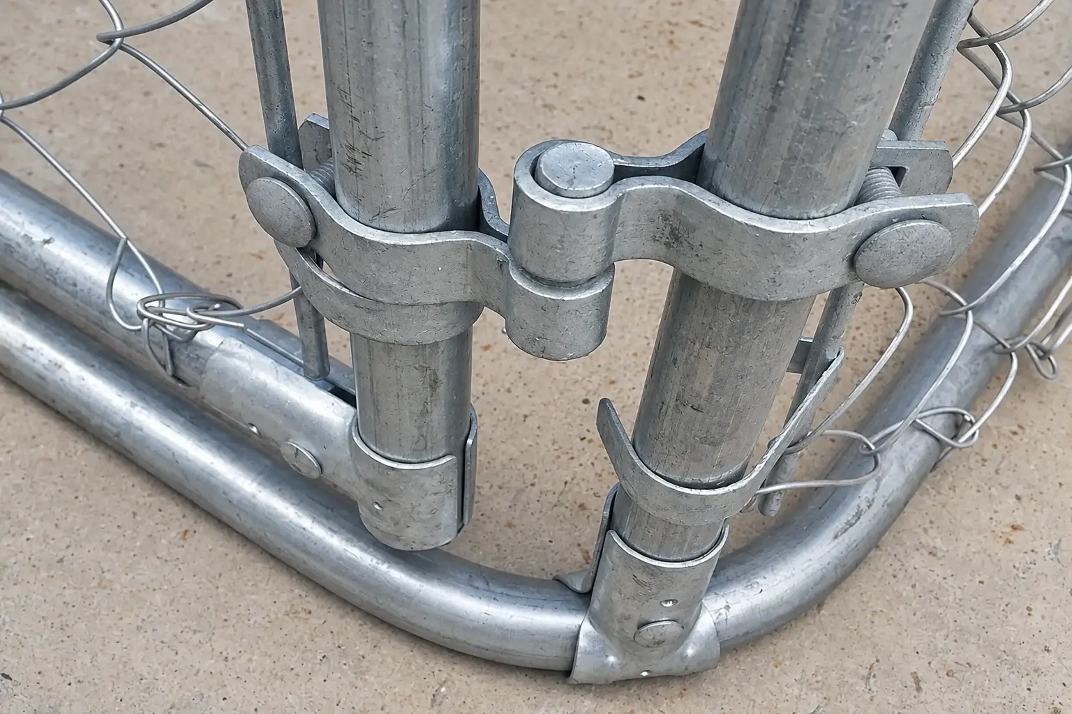 Galvanised clamp-on hinge joining two round tubes on a chain-link gate