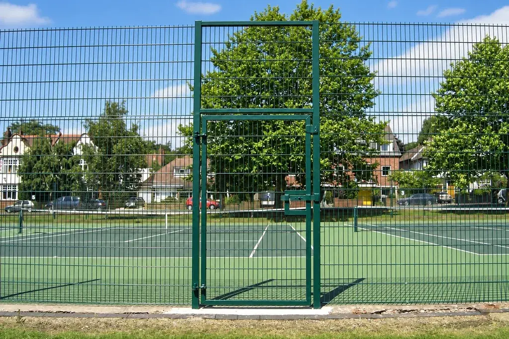 Green pedestrian gate in a tall tennis court mesh fence.