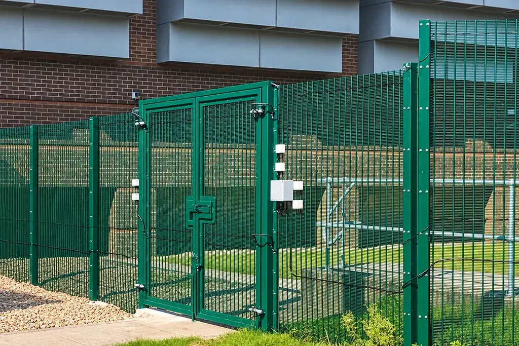 Green mesh fence and gate beside a water treatment facility.
