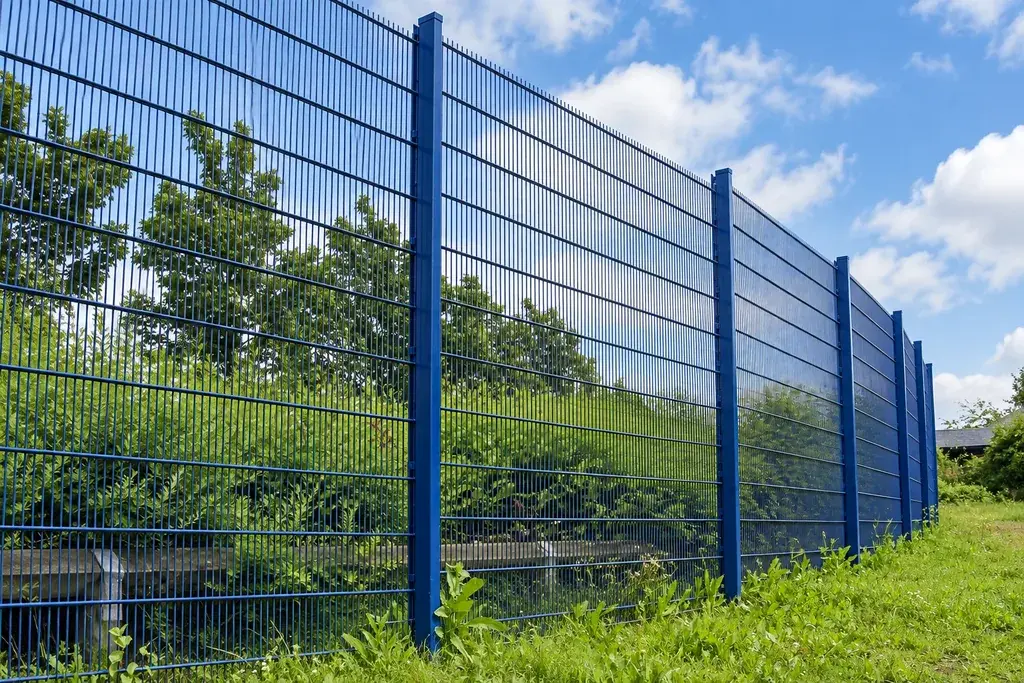 Blue double-wire fence panels and posts beside a planted boundary