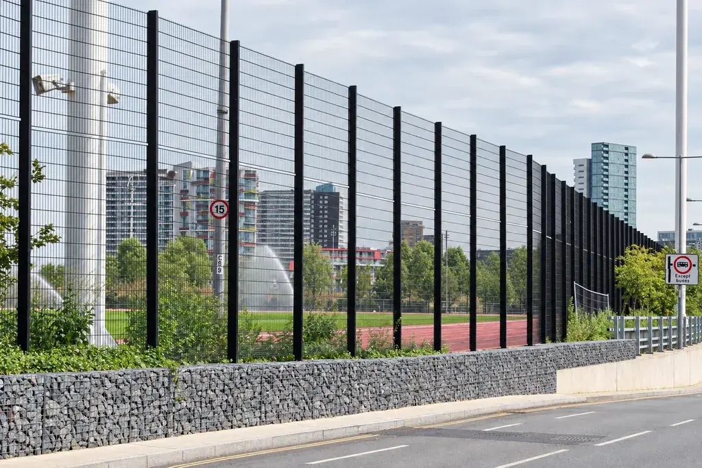 Double-wire fence panels mounted above a stone-filled boundary beside a road
